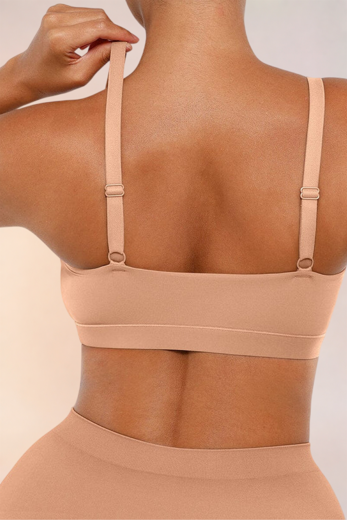 Skinzform Doux Bralette in Beige, back view - model lifting one adjustable strap